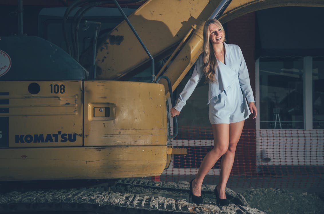 Photo of Laughing Woman In Blue Romper Holding While Standing on Excavator
